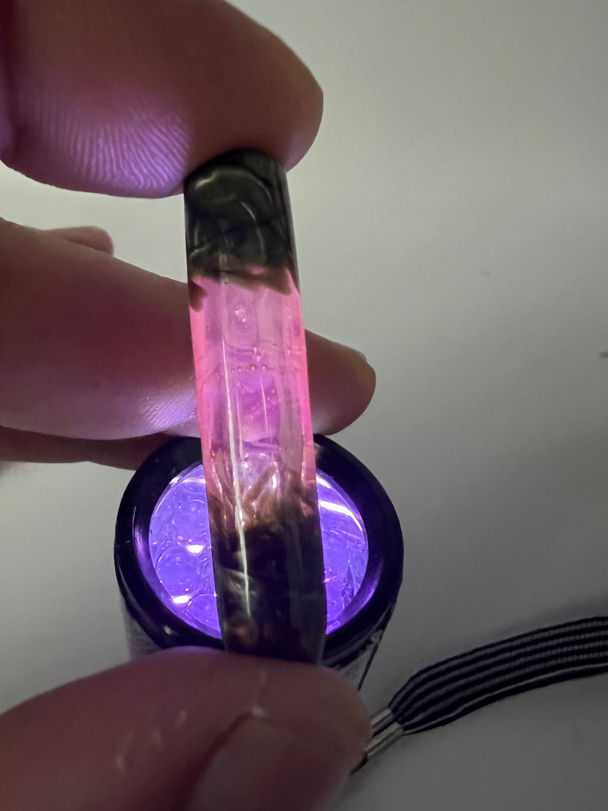 Boquilla de vidrio UV rosa y Electrum reaccionando bajo luz ultravioleta con brillo rosa fluorescente.
